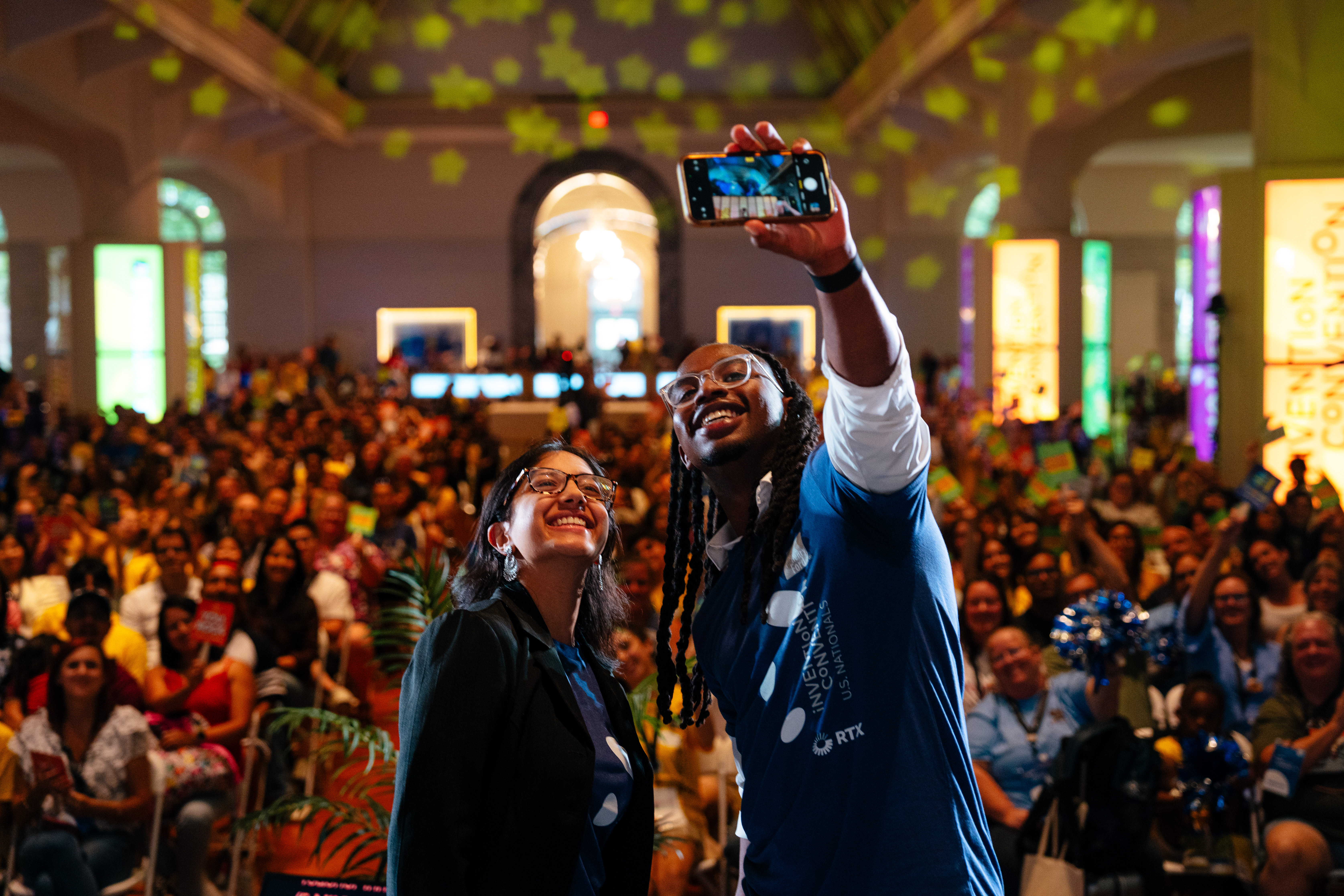 Two people stand in front of a crowd taking a selfie